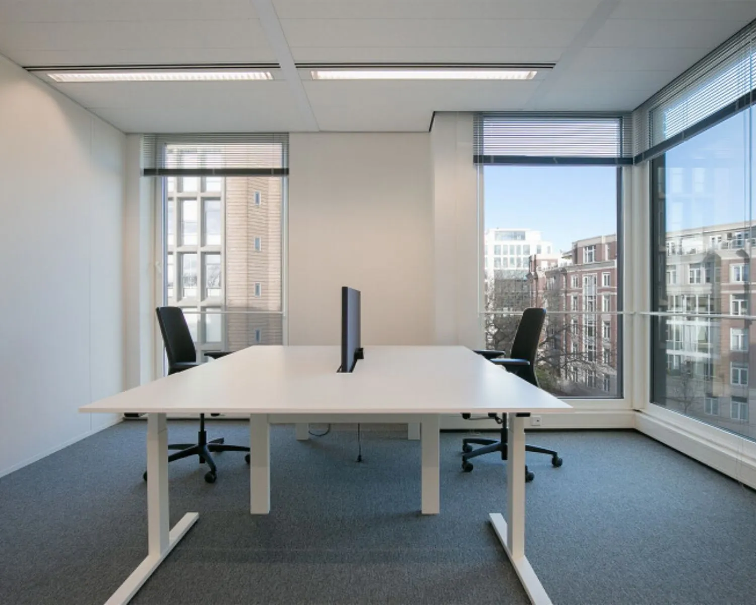 Moderne kantoorruimte te huur aan het Alexanderveld 5-13 in Den Haag met grote ramen en twee bureaus met bureaustoelen.