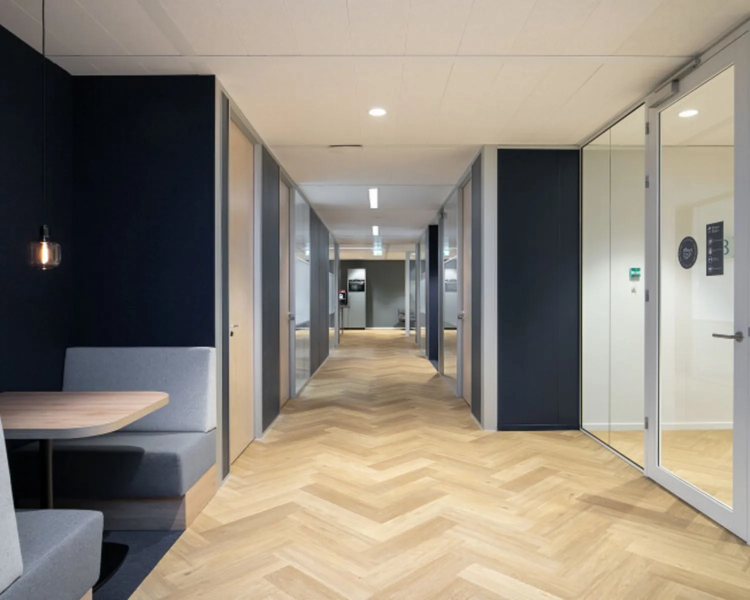 Moderne kantoorruimte aan het Alexanderveld 5-7 in Den Haag met glazen deuren, visgraatvloer en zitgedeelte.