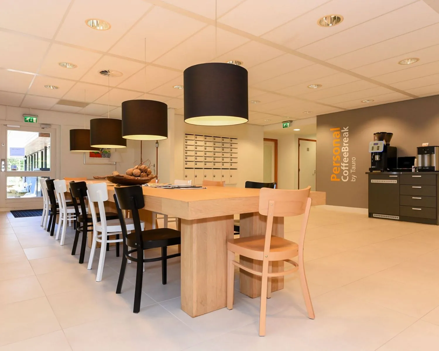 Moderne gemeenschappelijke kantoorruimte met lange houten tafel, verschillende stoelen, hanglampen en een koffiecorner in Heemstede aan de Herenweg 15.