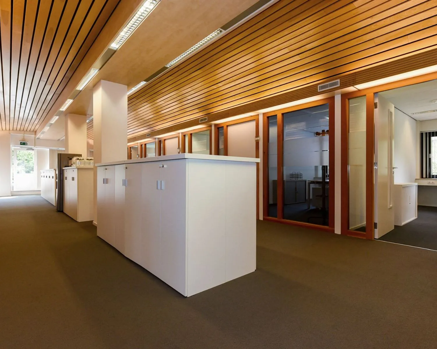 Moderne kantoorruimte aan de Herenweg 15 in Heemstede met glazen kantoorkamers, houten plafonddetails en witte opbergkasten.