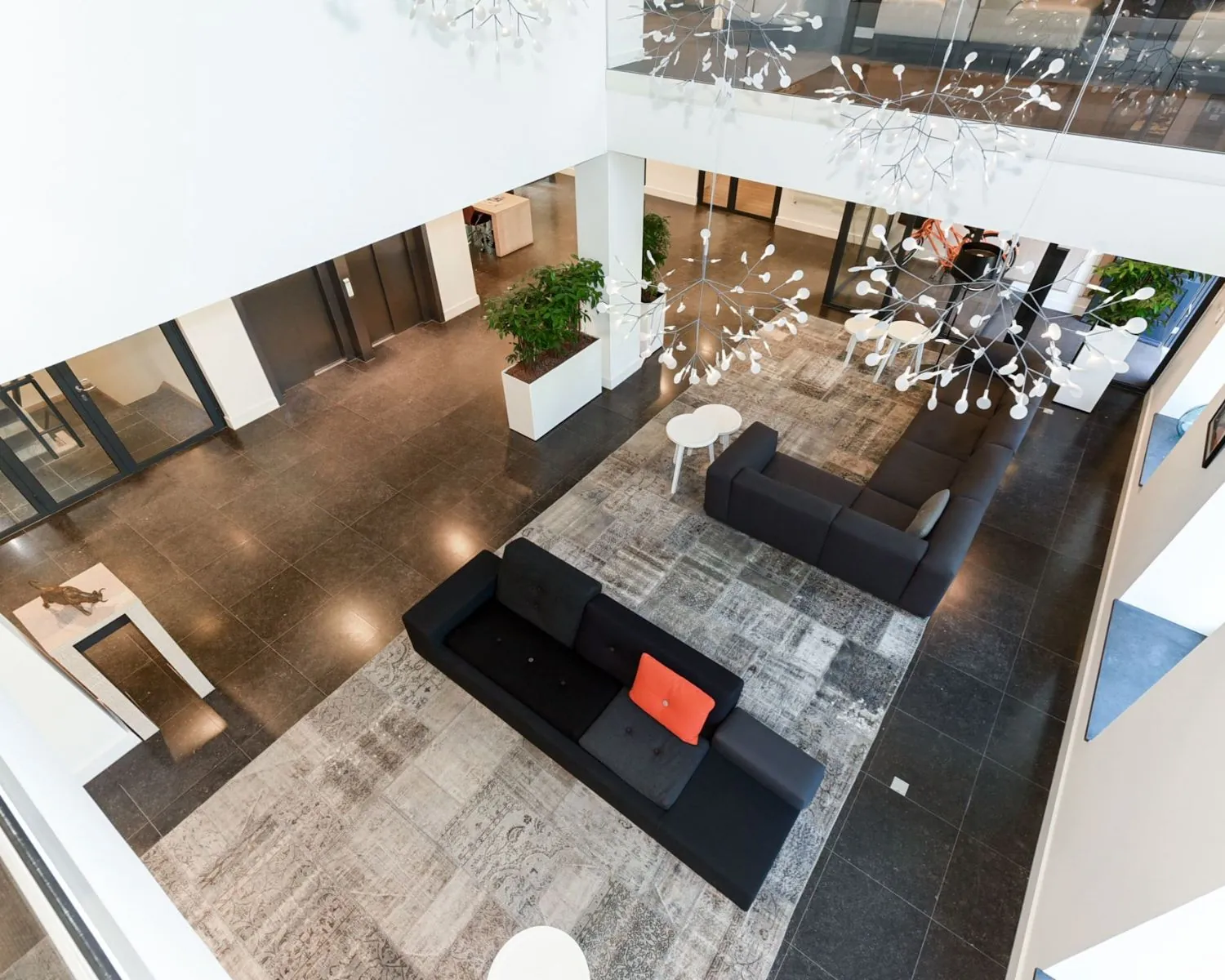 Moderne, open kantoorlobby aan de Koninginnegracht 19 in Den Haag met strakke meubels, grote vloerkleden en designverlichting.