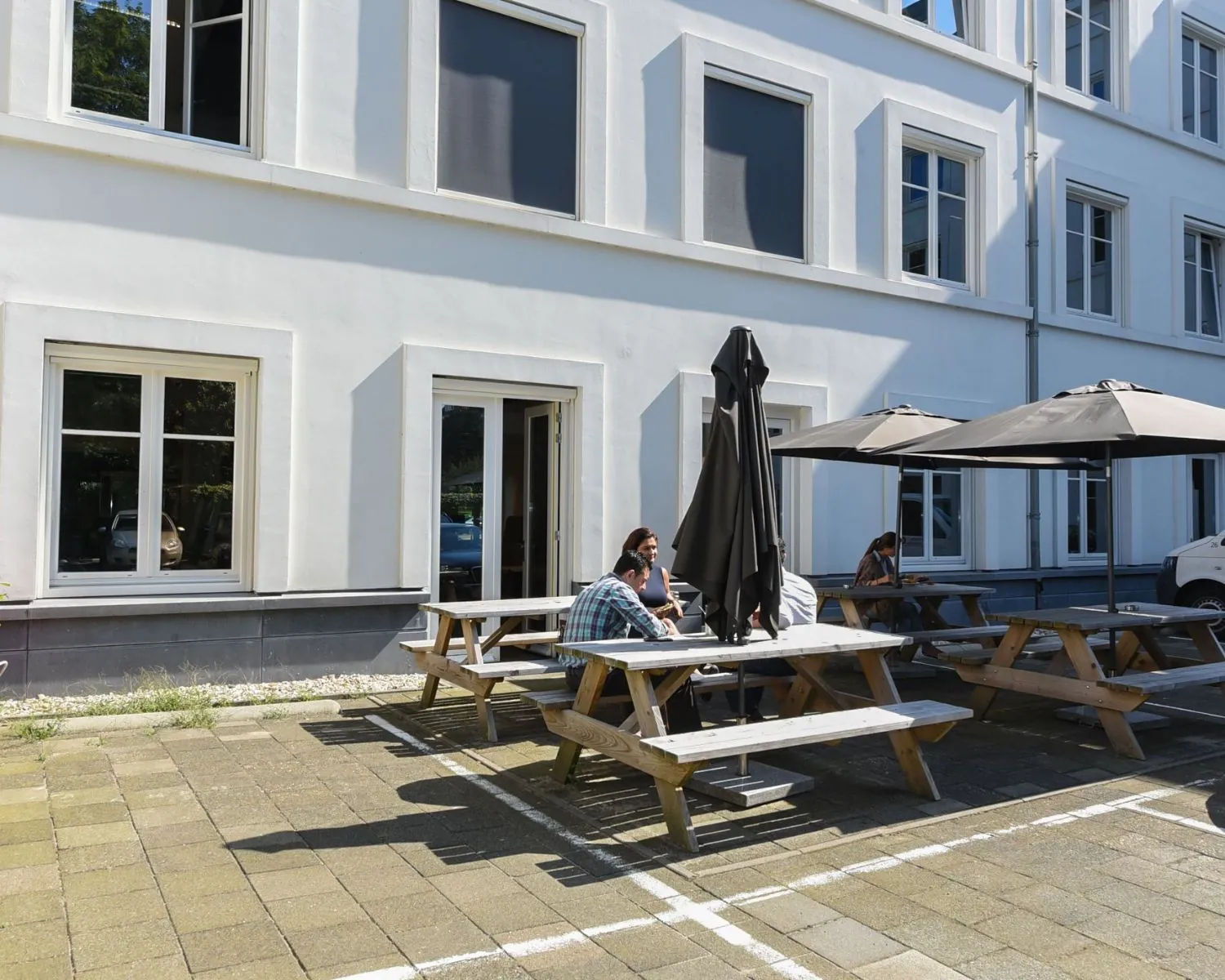 Buitenterras met picknicktafels en parasols bij kantoorruimte aan de Koninginnegracht 19 in Den Haag.