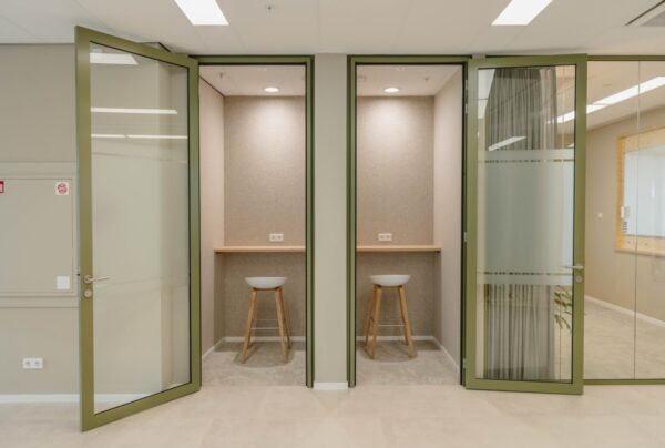 Twee kleine kantoorhokjes met barkrukken en glazen deuren in een kantoorruimte aan de Basisweg 30 in Amsterdam.