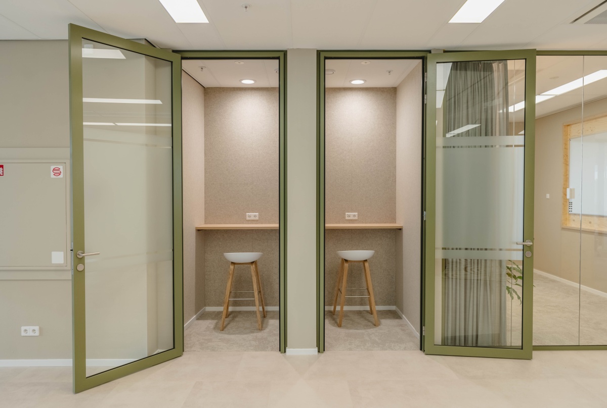 Twee kleine kantoorhokjes met barkrukken en glazen deuren in een kantoorruimte aan de Basisweg 30 in Amsterdam.