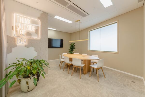 Moderne vergaderruimte in Amsterdam met een ronde houten tafel, zes stoelen, planten en een inspirerende neonmuurtekst.