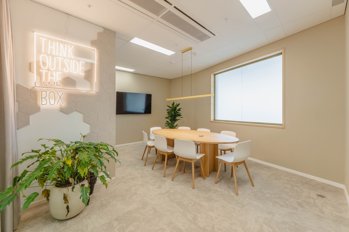 Moderne vergaderruimte in Amsterdam met een ronde houten tafel, zes stoelen, planten en een inspirerende neonmuurtekst.