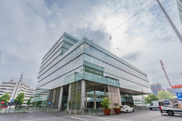 Modern kantoorgebouw met glazen gevels aan de Herikerbergweg in Amsterdam op een bewolkte dag.
