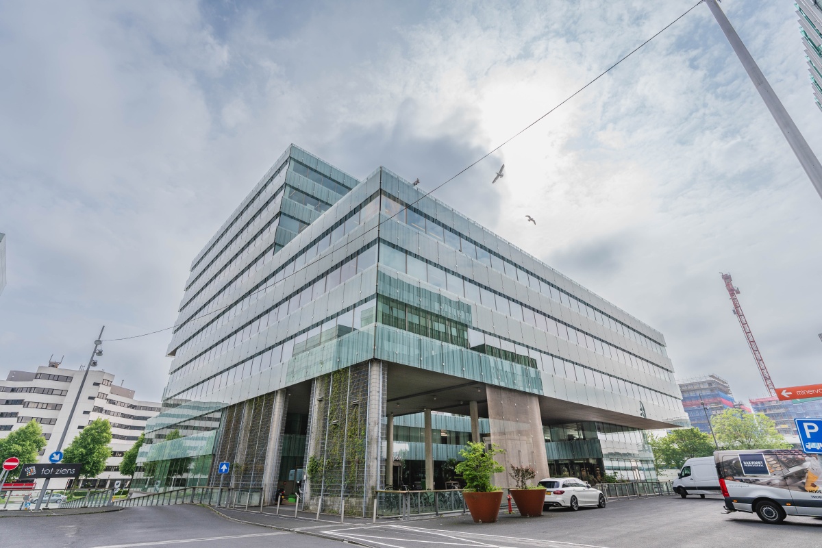 Modern kantoorgebouw met glazen gevels aan de Herikerbergweg in Amsterdam op een bewolkte dag.