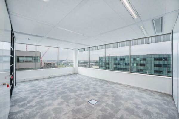 Lege kantoorruimte met grote ramen en uitzicht op gebouwen aan de Herikerbergweg in Amsterdam.