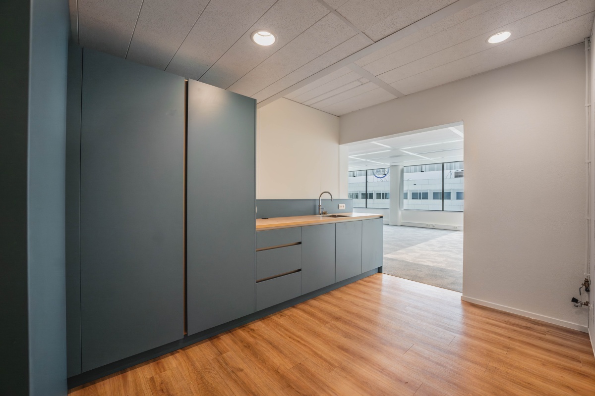 Moderne kantoorruimte met een kitchenette en grote ramen aan de Herikerbergweg in Amsterdam.