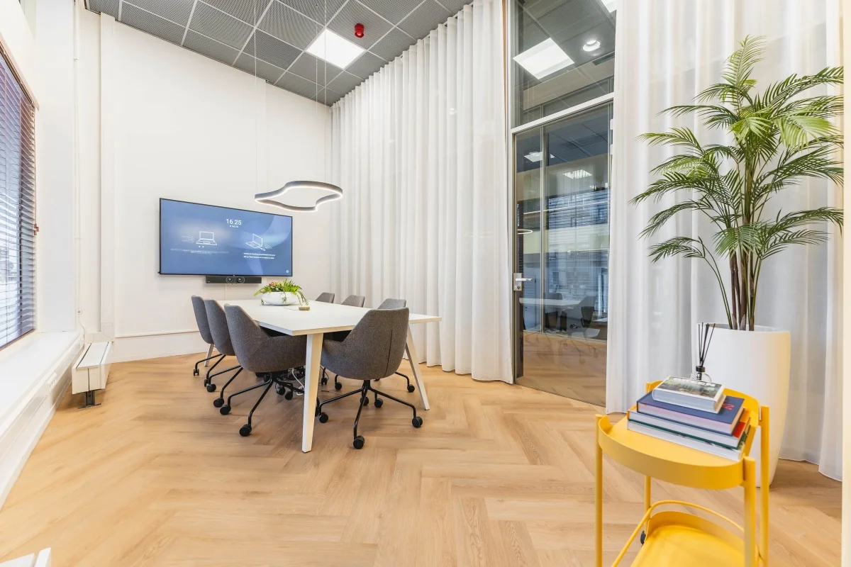 Moderne vergaderruimte aan de Weesperstraat 107-121 in Amsterdam met een conferentietafel, designstoelen, presentatiescherm en grote raampartijen met witte gordijnen.