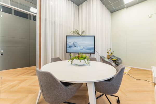 Moderne vergaderruimte aan de Weesperstraat in Amsterdam met ronde tafel, grijze stoelen, flatscreen en decoratieve planten.