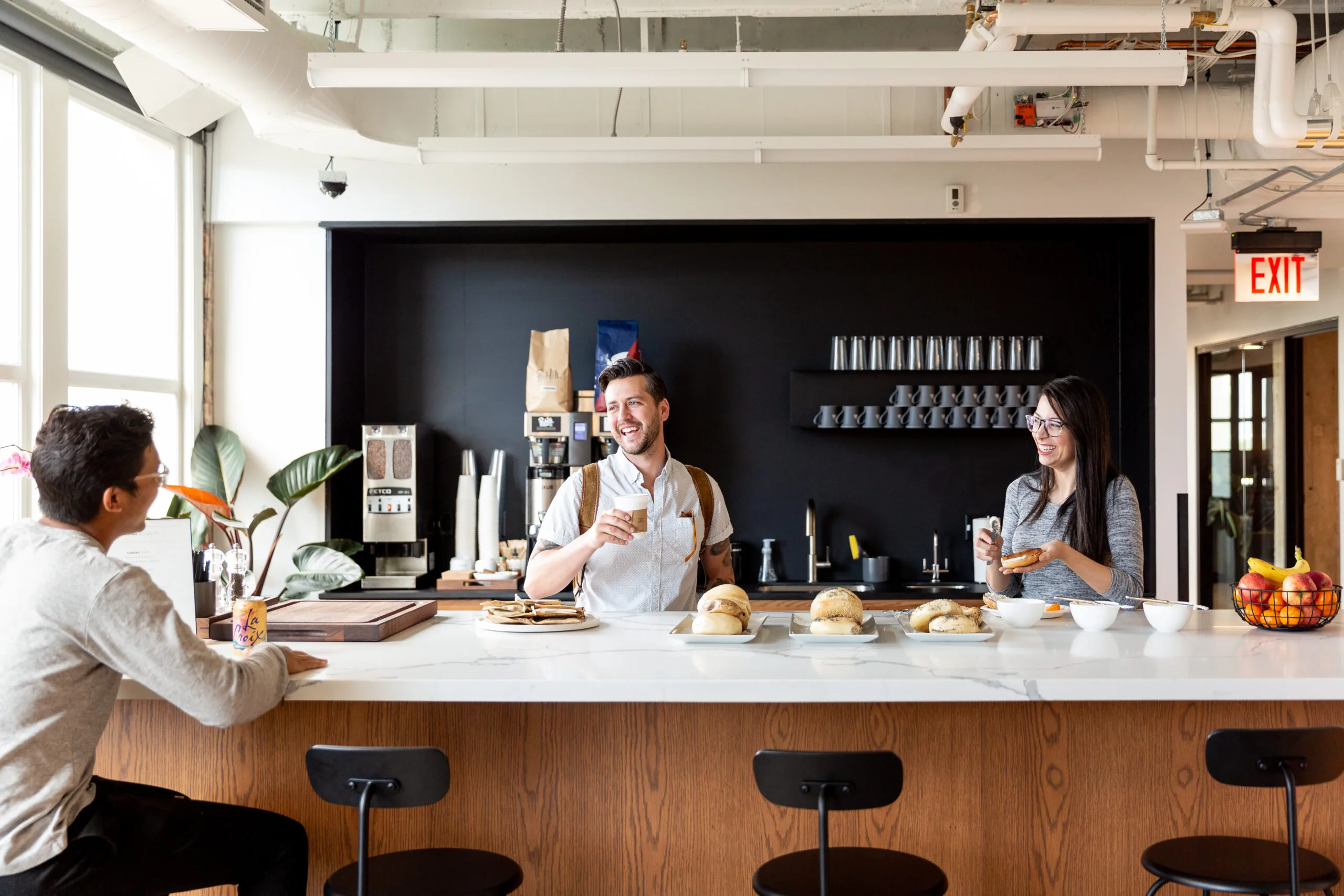Drie mensen praten en lachen samen in een moderne kantoorkeuken op Burgerweeshuispad 301 in Amsterdam.