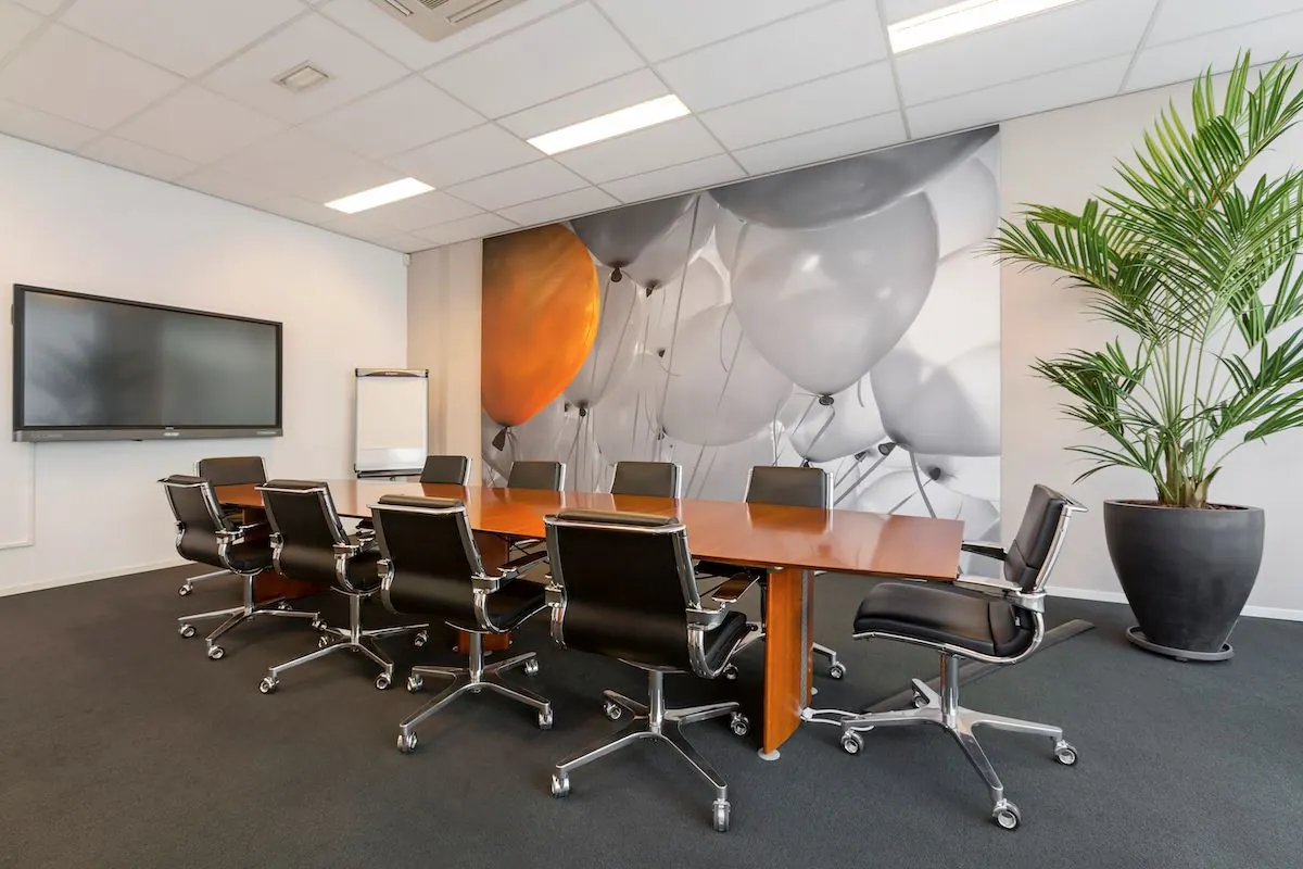 Moderne vergaderruimte aan de Leeghwaterstraat 25 in Reeuwijk met een lange houten tafel, zwarte bureaustoelen, grote muurfoto met ballonnen en een flatscreen.