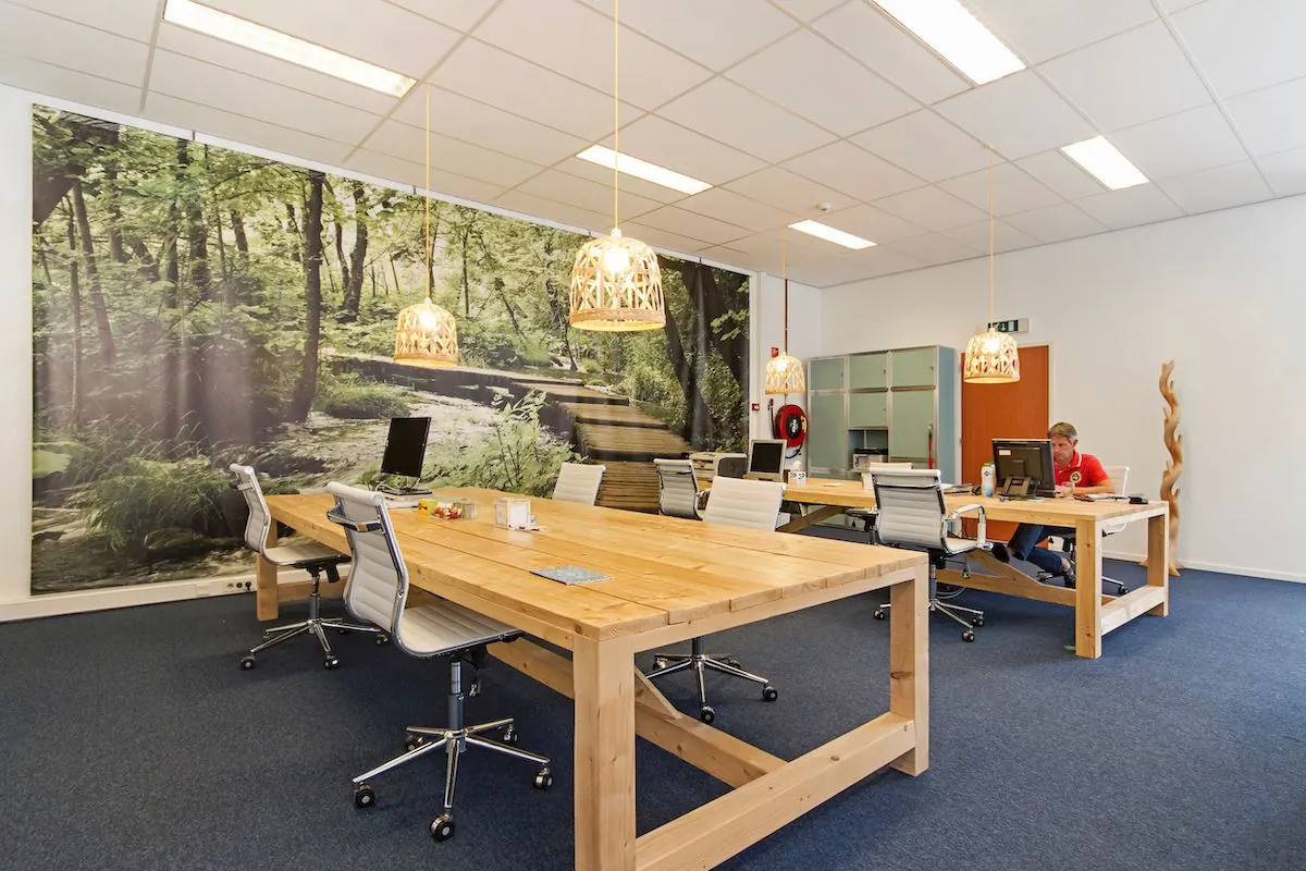 Moderne kantoorruimte aan de Leeghwaterstraat 25 in Reeuwijk met houten bureaus, ergonomische stoelen en een fotowand met boslandschap.