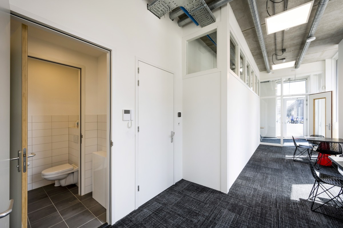 Moderne kantoorruimte met openstaande deur naar toilet en kantoor, minimalistische inrichting.