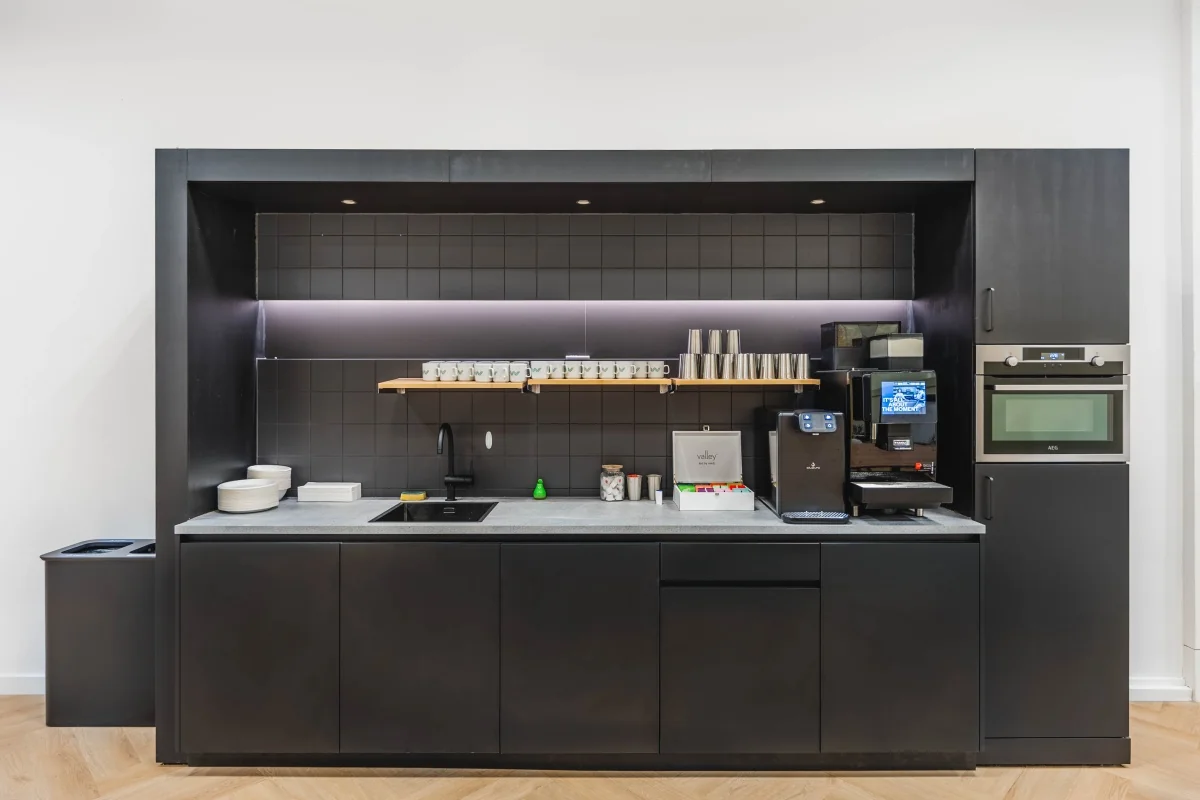 Moderne kantoorkeuken met ingebouwde apparatuur, koffieautomaat en strakke zwarte afwerking aan de Weesperstraat 107.