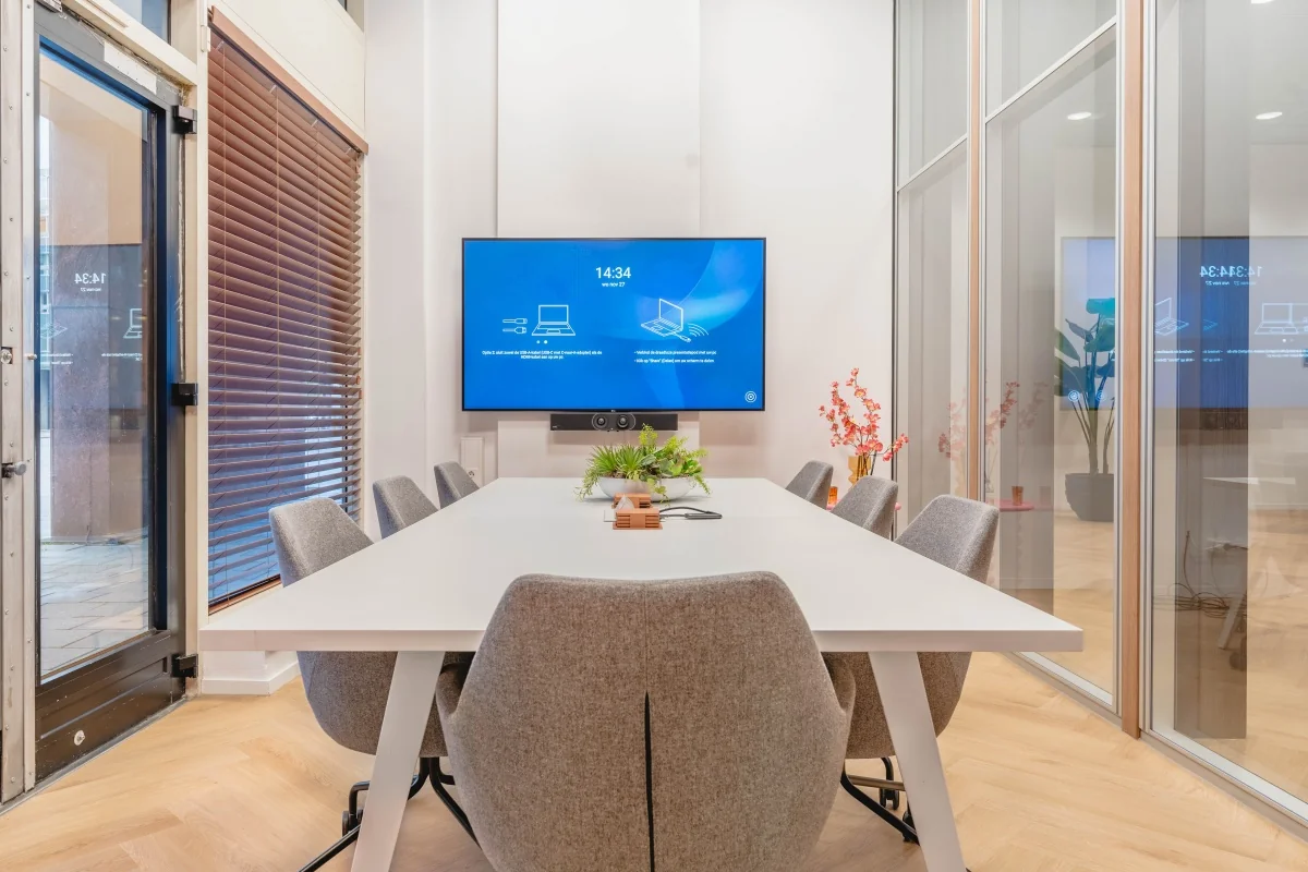 Moderne vergaderruimte aan de Weesperstraat 107 met grote tafel, grijze stoelen en een scherm aan de muur.