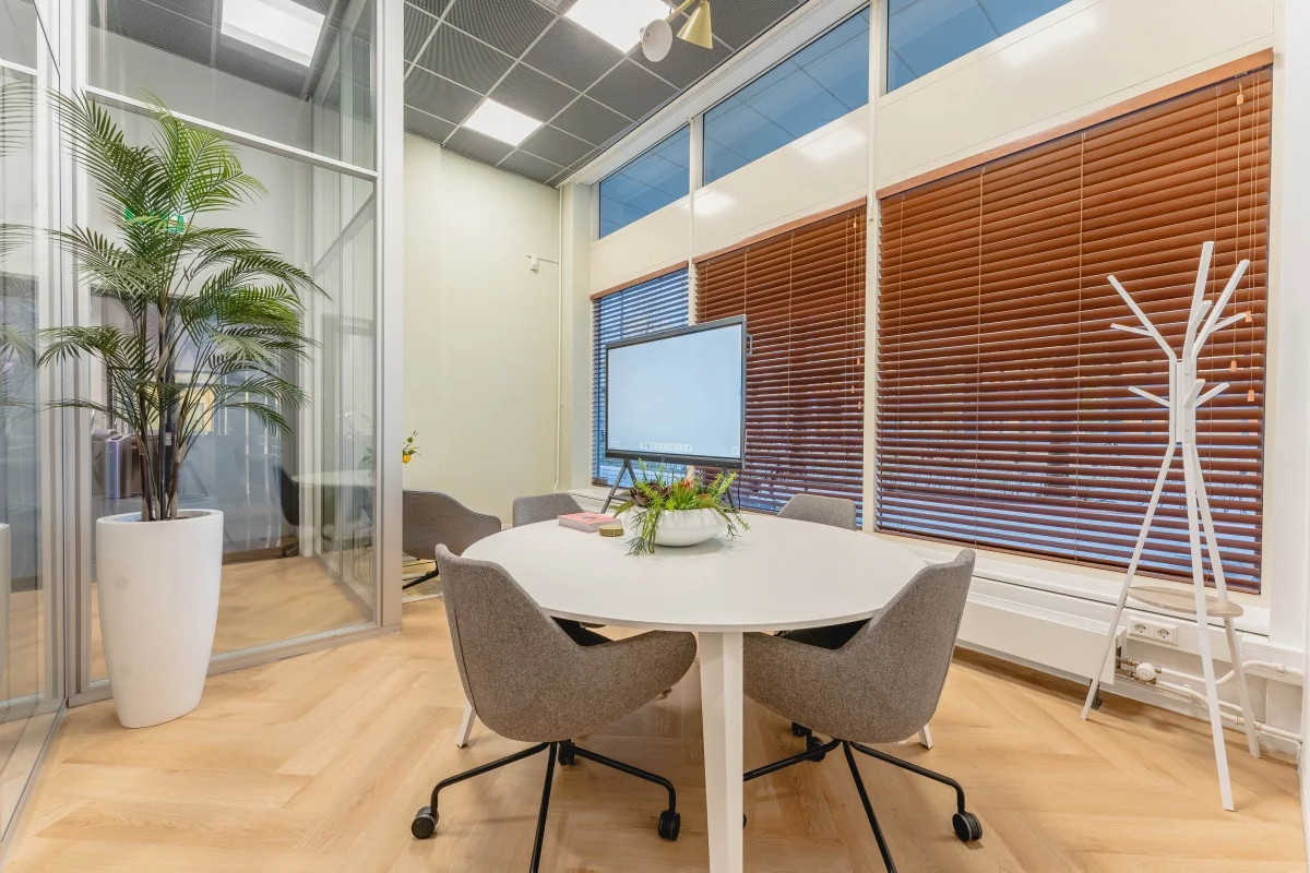 Moderne vergaderruimte aan de Weesperstraat 107 met ronde tafel, flatscreen, grijze stoelen en houten jaloezieën.