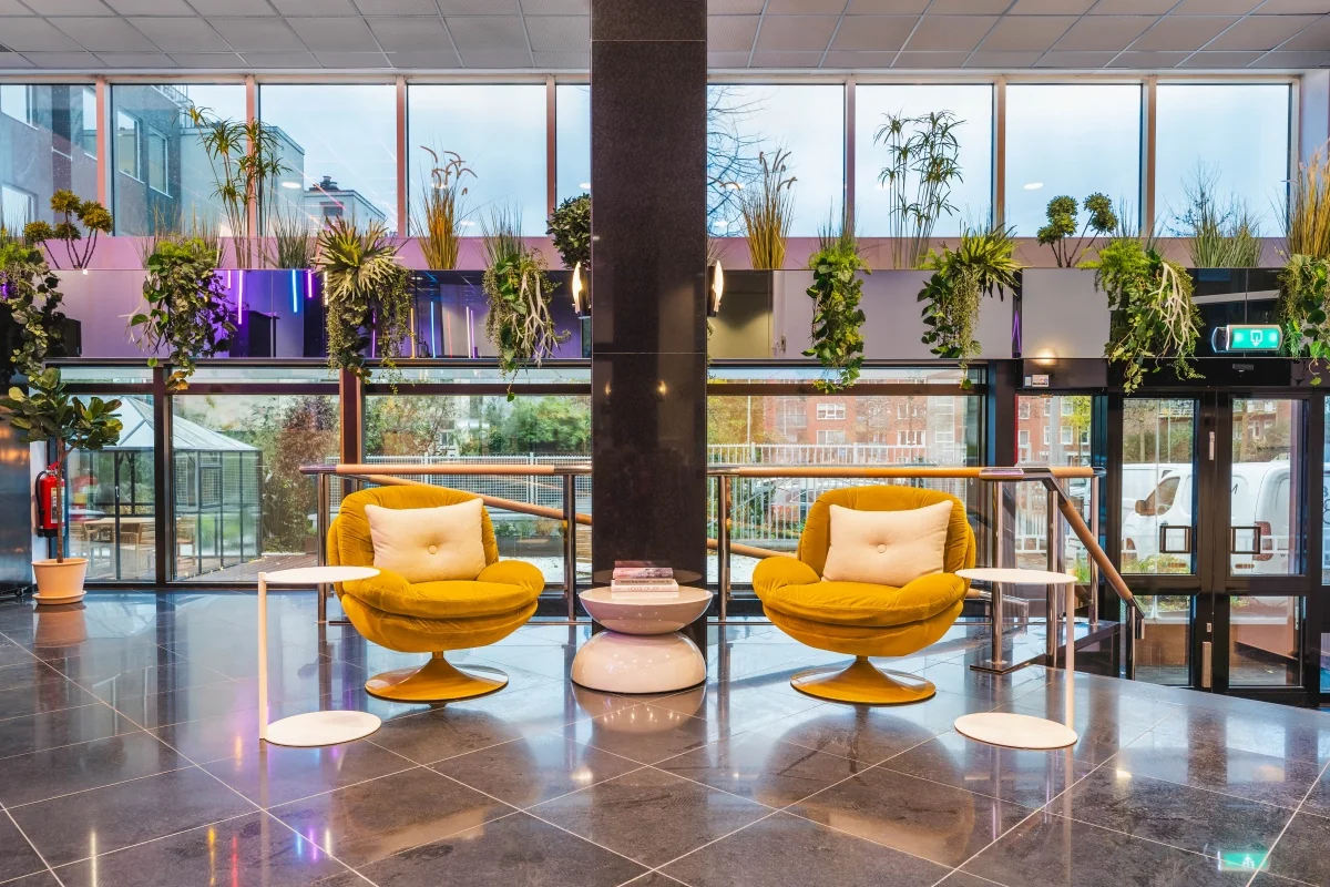 Moderne en kleurrijke loungehoek met gele fauteuils en veel groen in de entree van een kantoorpand aan de Weesperstraat 107.