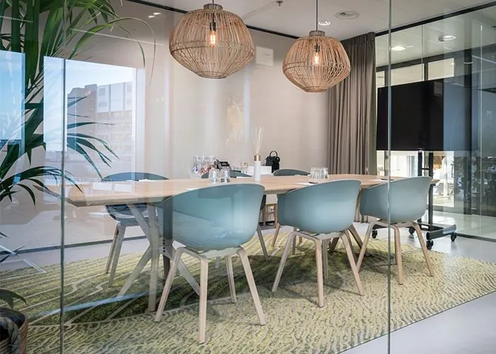 Moderne vergaderruimte met lichtblauwe stoelen en houten tafel in een glazen kantoor aan het Wilhelminaplein 1 in Rotterdam.
