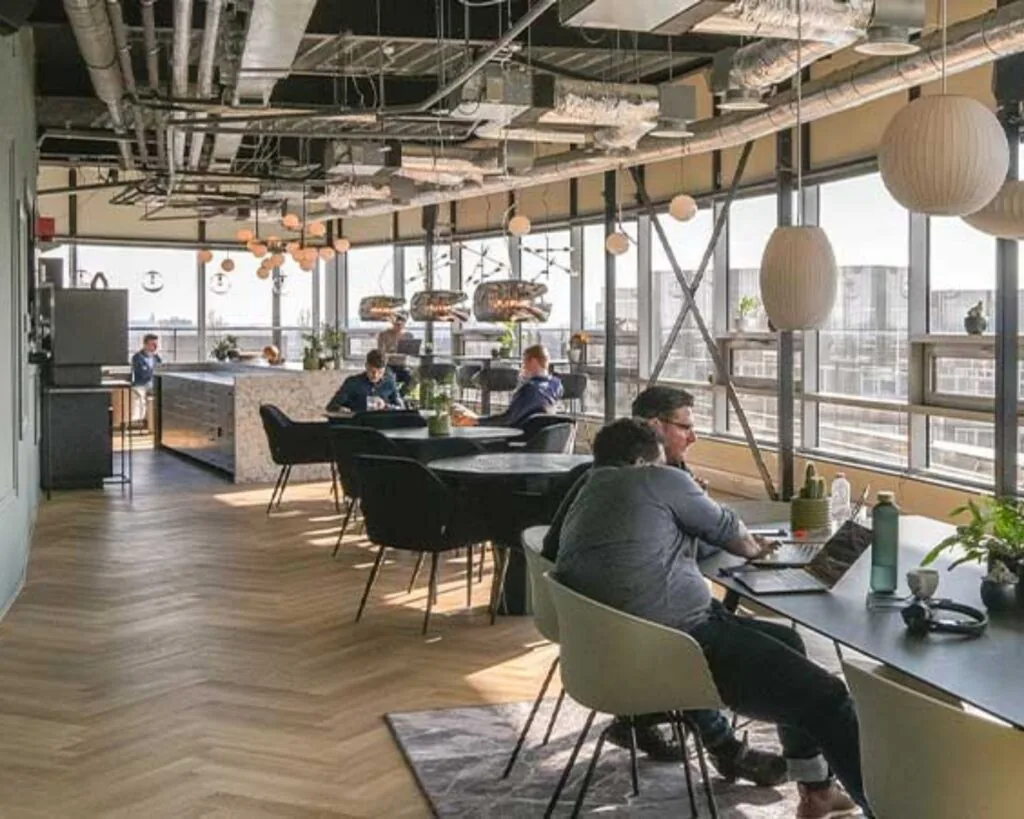 Moderne, lichte kantoorruimte aan het Bos en Lommerplein in Amsterdam met open werkplekken, grote ramen en een gezamenlijke keukenruimte.