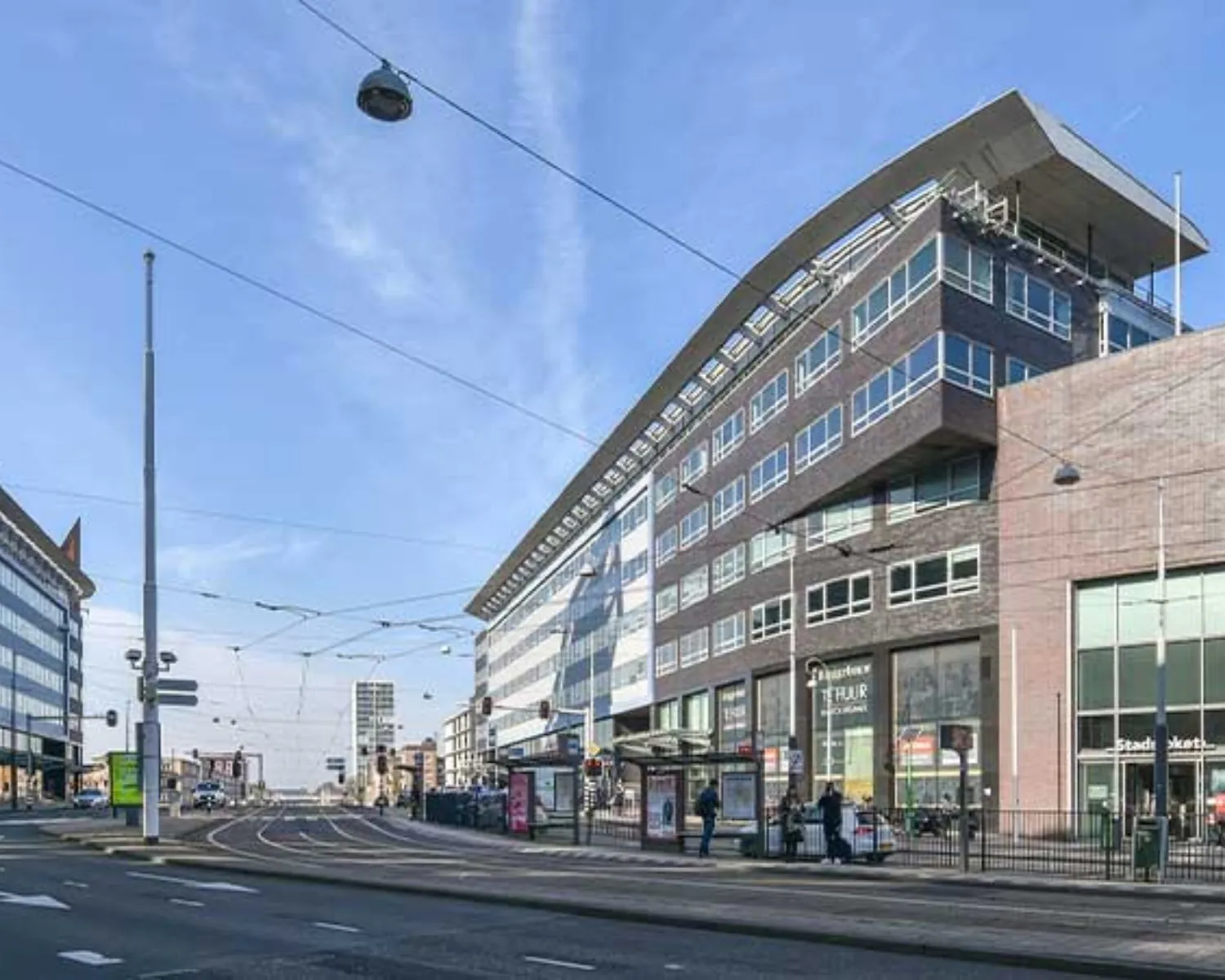 Modern kantoorgebouw aan het Bos en Lommerplein in Amsterdam met tramhalte en bushokje op de voorgrond.
