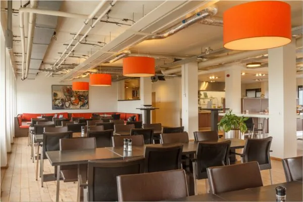 Moderne en ruime kantine met oranje hanglampen en donkerbruin meubilair in een kantoorruimte aan Bredewater 26 in Zoetermeer.