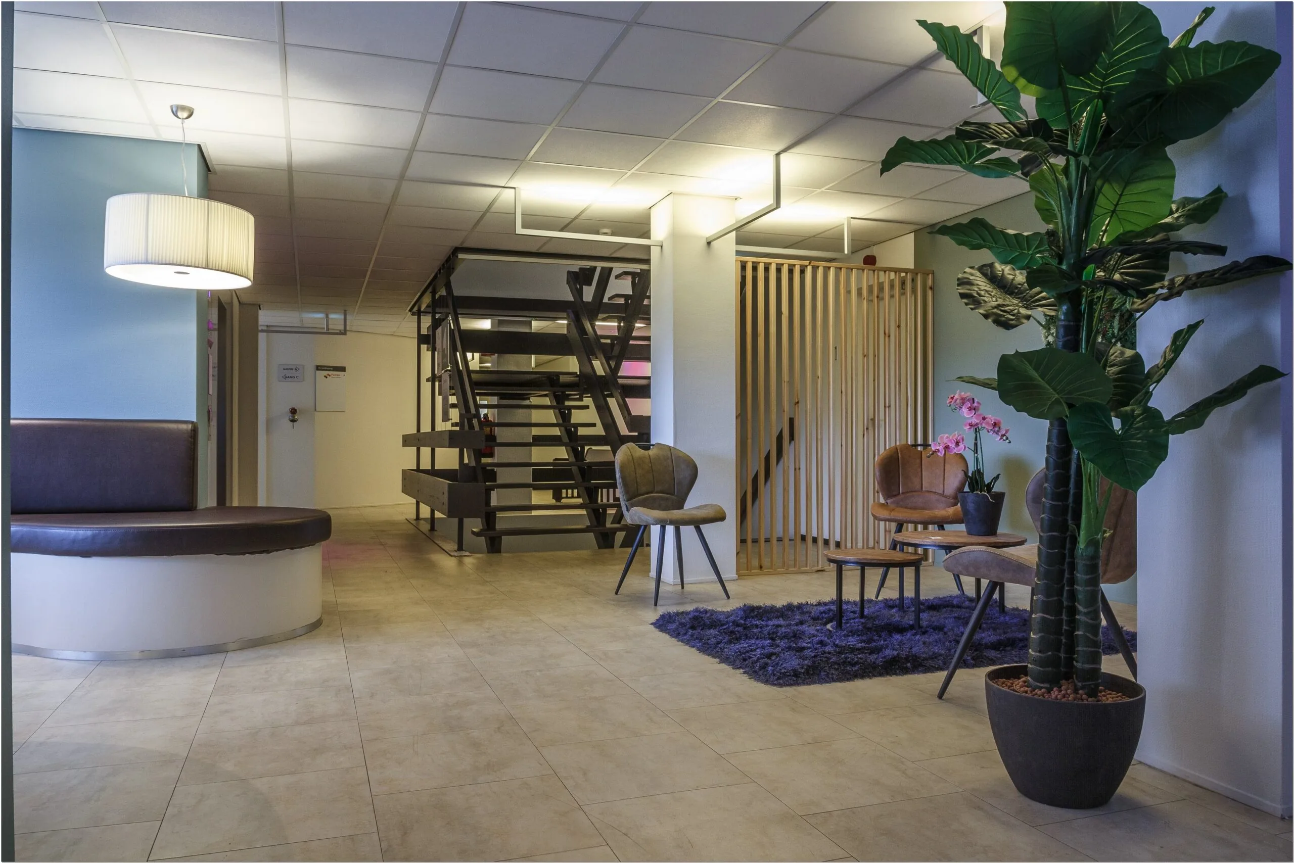 Moderne wachtruimte in kantoorruimte aan Bredewater 26 in Zoetermeer met zitgelegenheid, kunstplanten en een stalen trap.