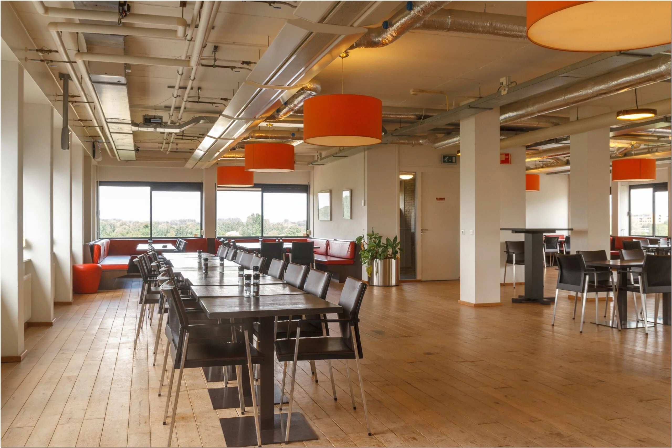 Moderne, open kantoorruimte met grote ramen, houten vloer, zwarte tafels en oranje hanglampen aan de Bredewater 26 in Zoetermeer.