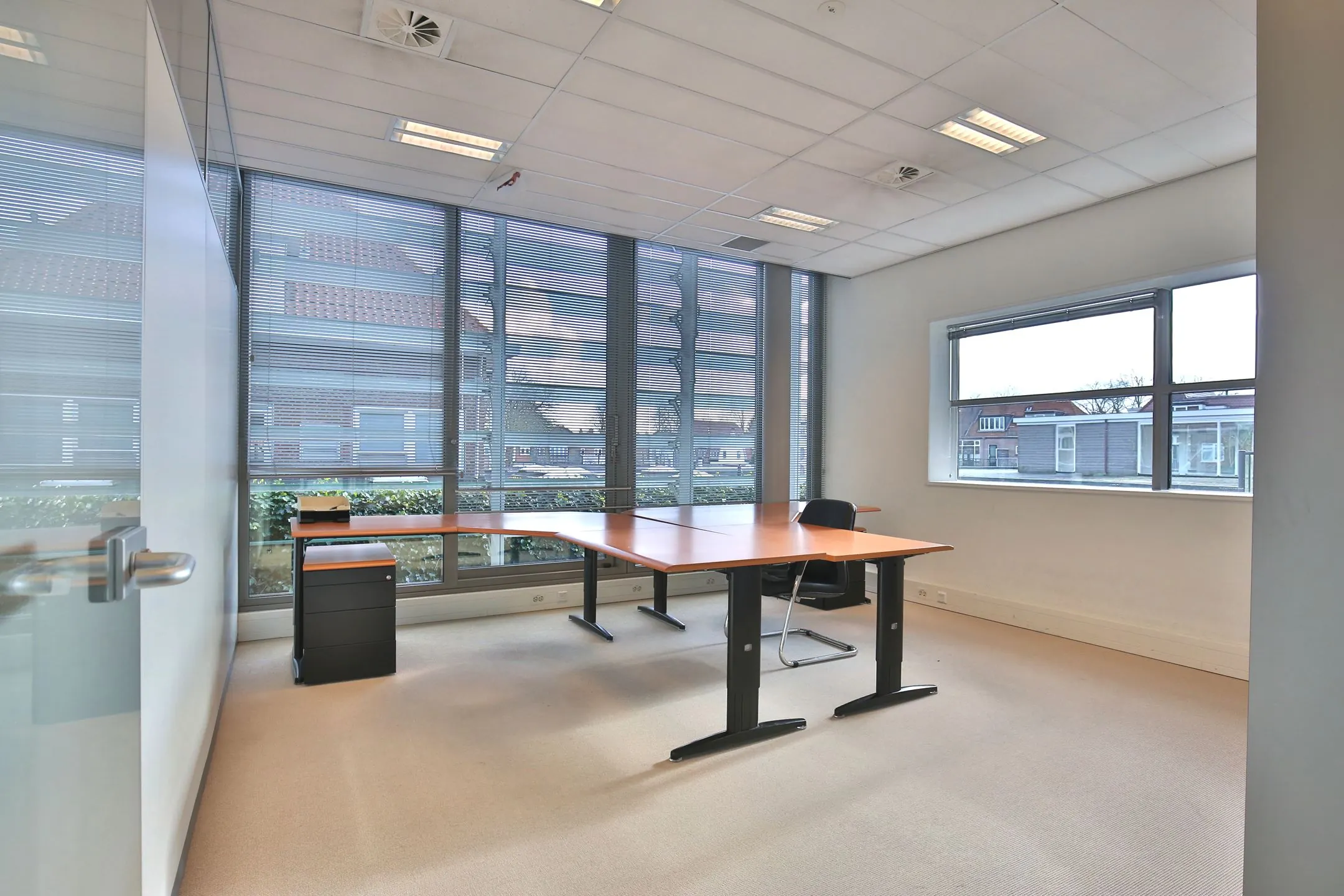 Moderne, lichte kantoorruimte met grote ramen en een hoekbureau aan de Bronsteeweg 10 in Heemstede.
