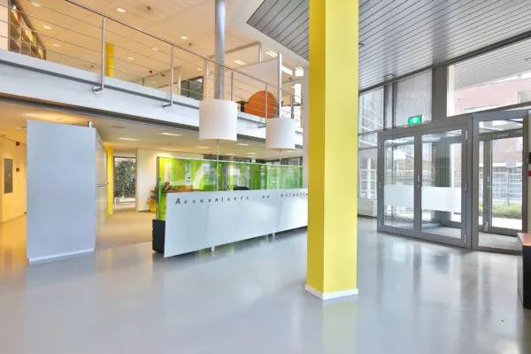 Moderne entree van een kantoorruimte aan de Bronsteeweg 10 in Heemstede met balie, glazen deuren en gele accenten.