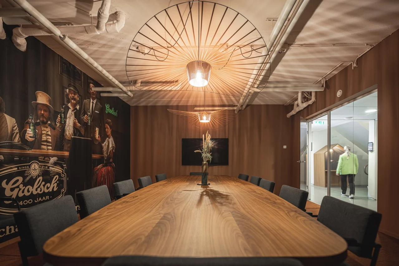 Vergaderruimte aan de Brouwerijstraat 1 in Enschede met lange houten tafel, moderne verlichting en Grolsch-muurdecoratie.