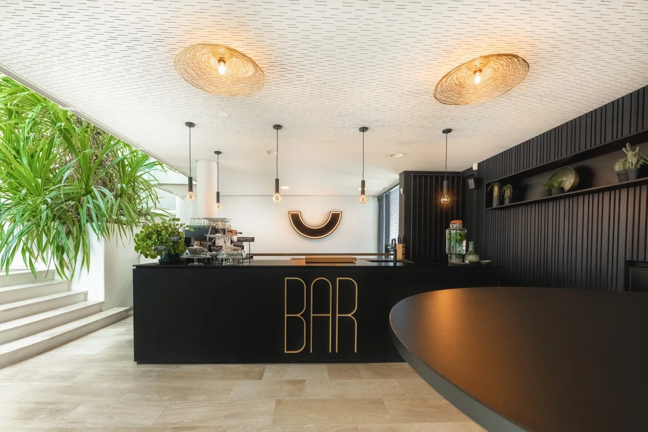Moderne kantoorbar met zwart interieur, hanglampen en groene planten aan de Brouwerijstraat 1 in Enschede.