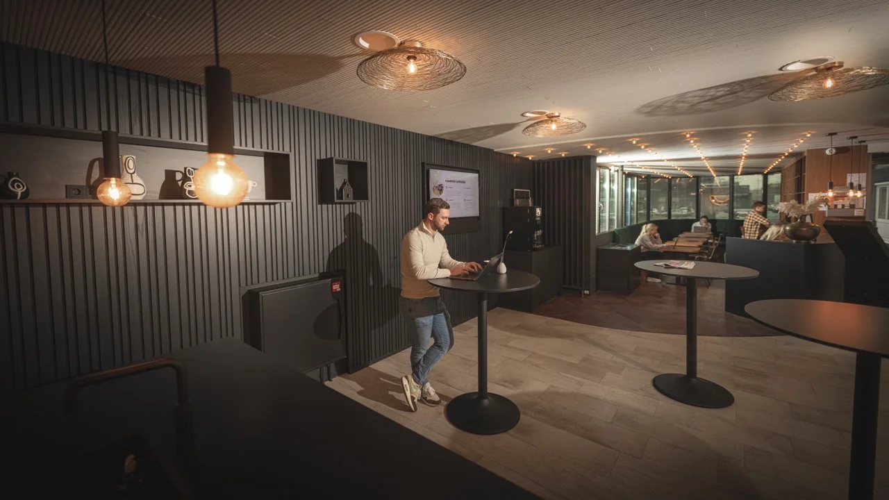 Moderne kantoorruimte aan de Brouwerijstraat 1 in Enschede met sta-tafels, sfeerverlichting en een loungegedeelte op de achtergrond.