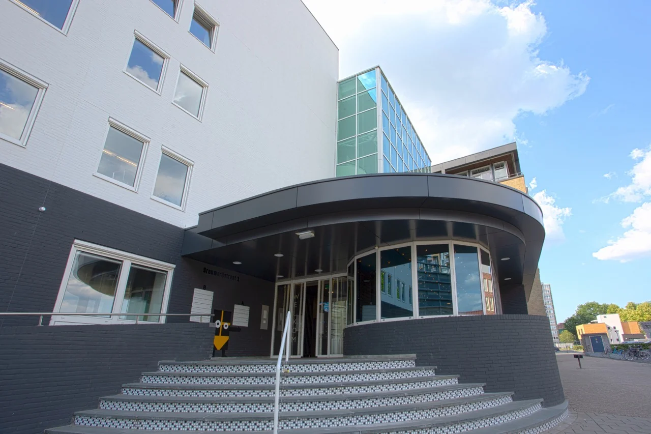 De entree van een modern kantoorgebouw aan de Brouwerijstraat 1 in Enschede met ronde trap en glazen gevel.