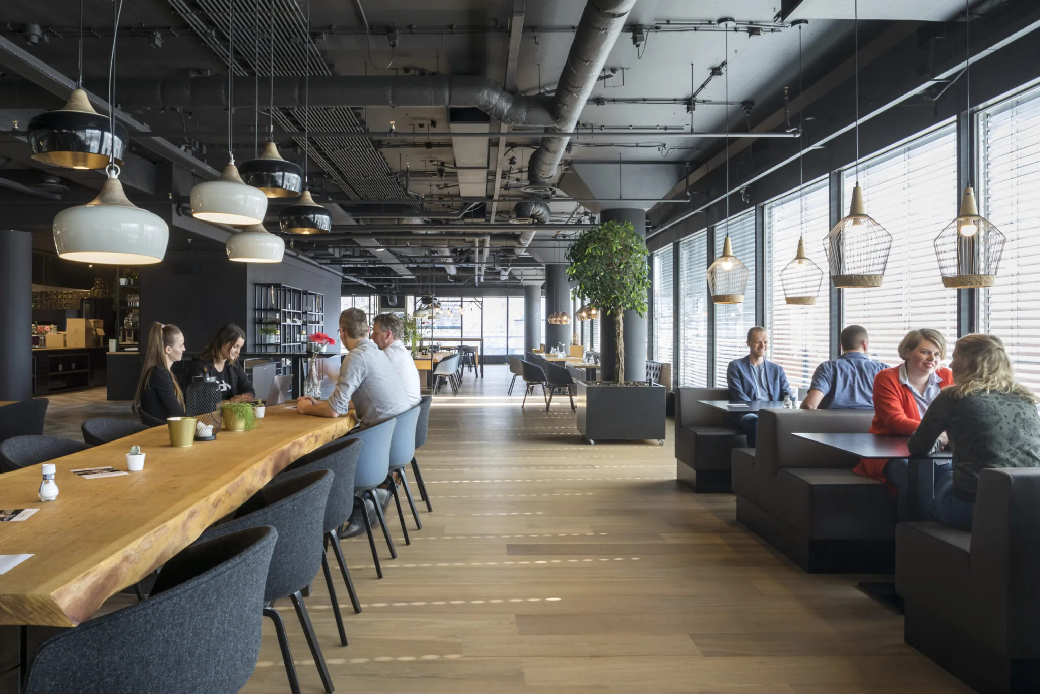 Moderne en open kantoorruimte in Flight Forum 760 in Eindhoven met zitplekken, grote houten tafels en sfeervolle verlichting.