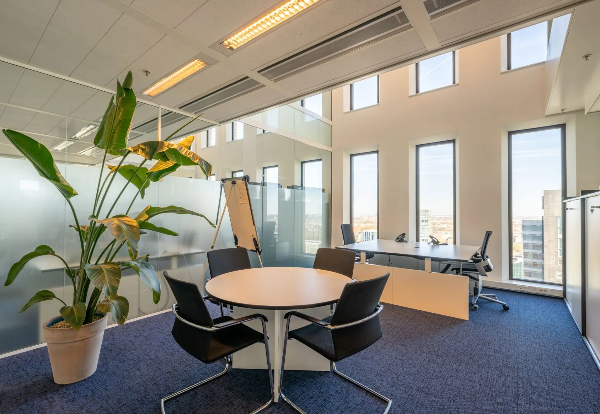 Moderne, lichte kantoorruimte met vergadertafel, bureau en grote ramen aan het Gustav Mahlerplein 109 in Amsterdam.