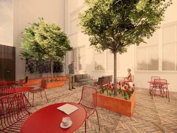 Zonnige binnentuin met rode zitjes, bloemenbakken en twee personen bij kantoorruimte aan de Keizersgracht 264 in Amsterdam.