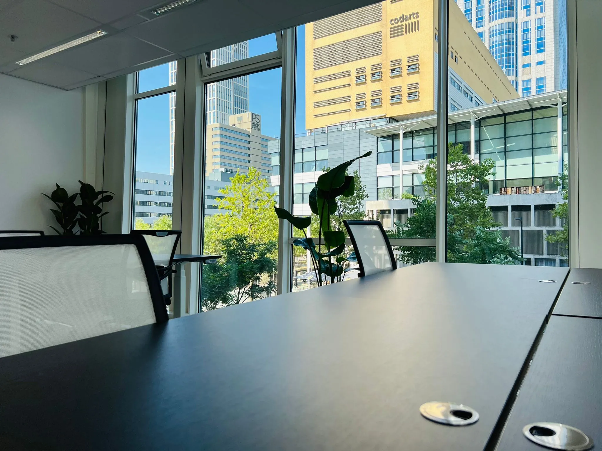 Moderne kantoorruimte met vergadertafel en stoelen, met uitzicht op gebouwen aan het Kruisplein in Rotterdam.