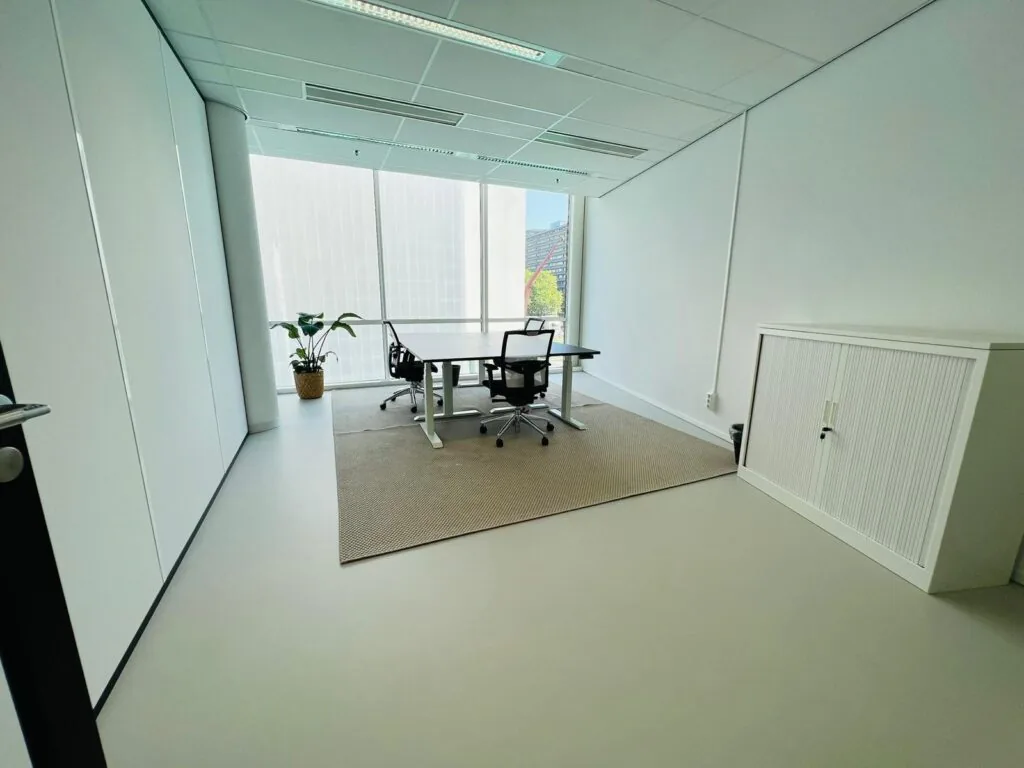 Moderne, lichte kantoorruimte aan het Kruisplein 480 in Rotterdam met bureau, stoelen, kast en grote ramen.