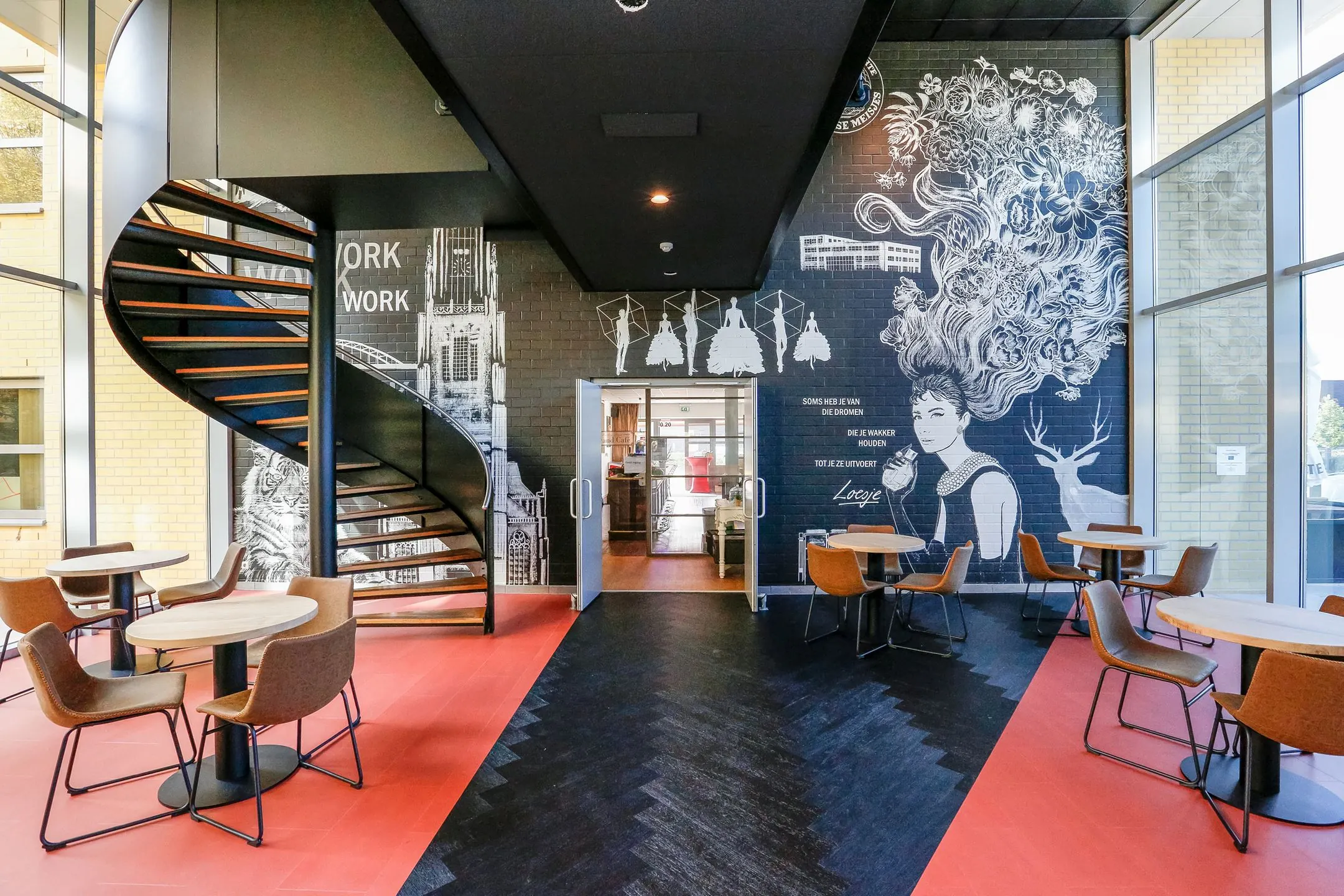 Moderne kantoorruimte aan de Meander 251 in Arnhem met een opvallende muurschildering, ronde zitjes en een zwarte wenteltrap.