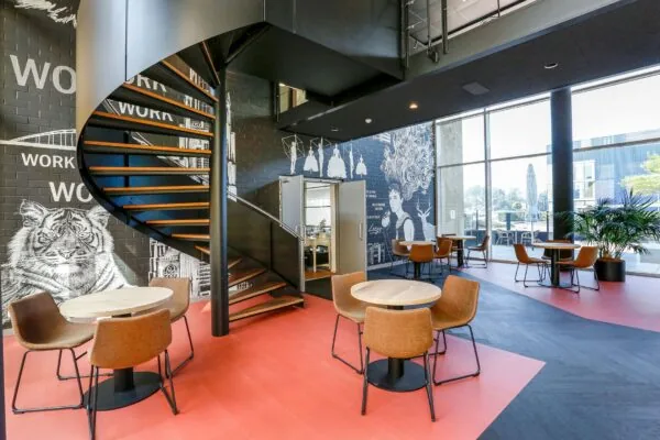 Moderne kantoorruimte in Meander 251 Arnhem met ronde zitjes, een zwarte wenteltrap en opvallende muurschilderingen.