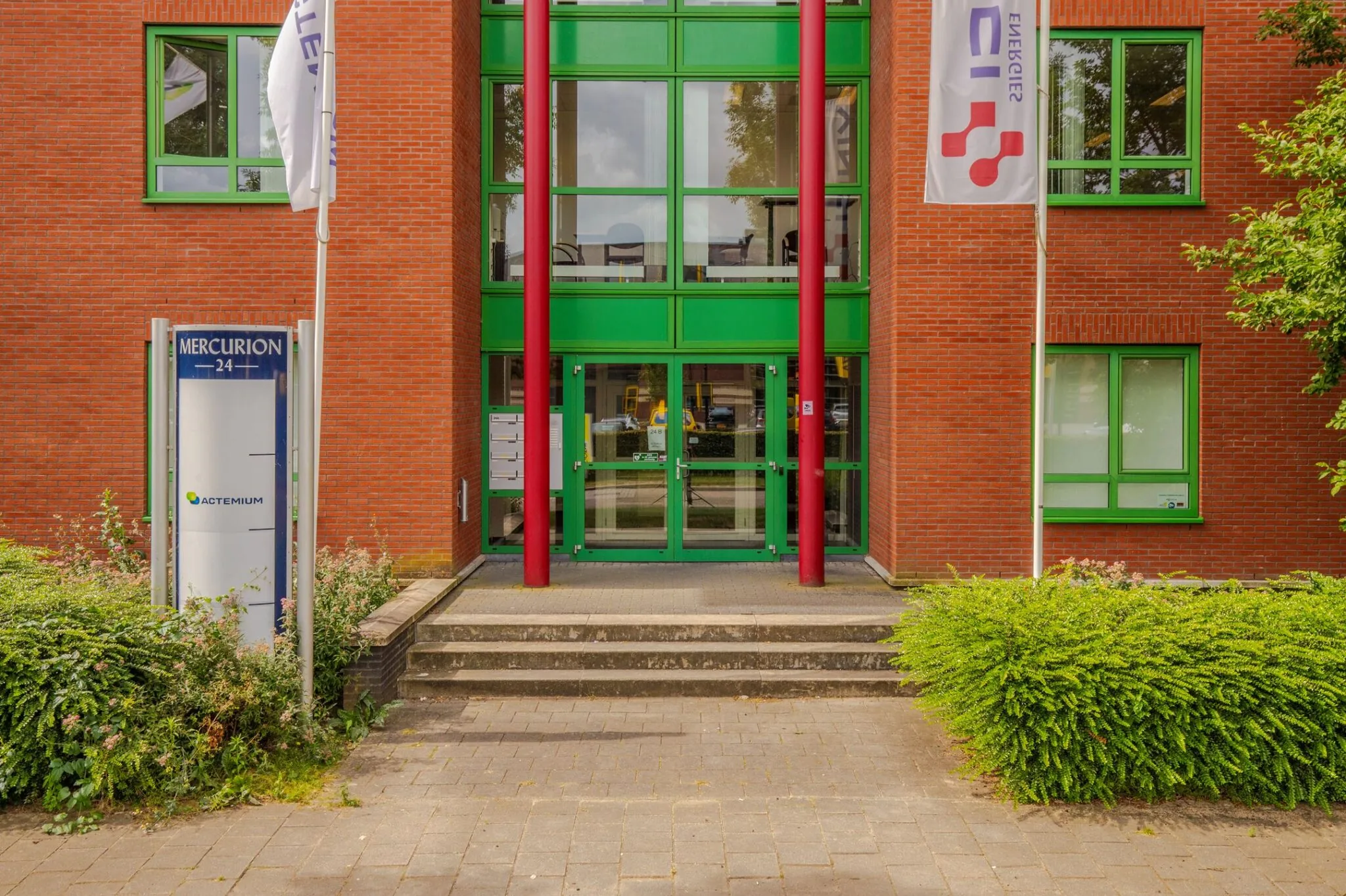 Ingang van het kantoorpand Mercurion 24 in Zevenaar met rood metselwerk, groene kozijnen en bedrijfsnaambord.