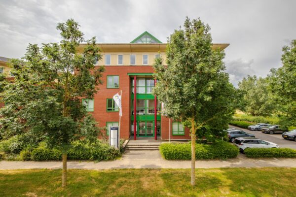 Vooraanzicht van het kantoorgebouw Mercurion 24 in Zevenaar met entree, vlaggenmast en omliggende parkeerplaatsen.