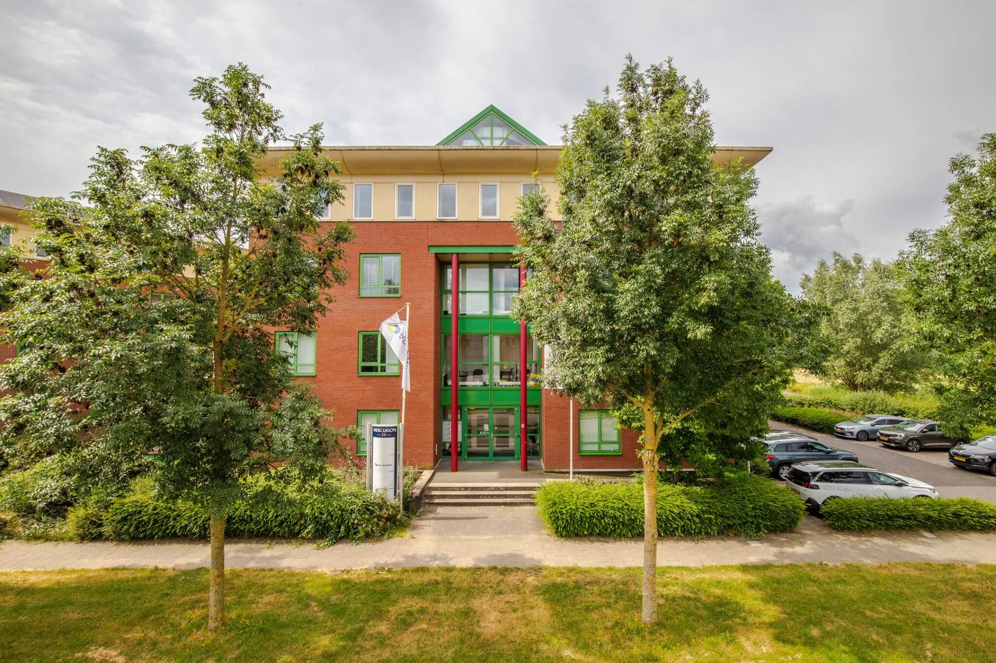 Vooraanzicht van het kantoorgebouw Mercurion 24 in Zevenaar met entree, vlaggenmast en omliggende parkeerplaatsen.