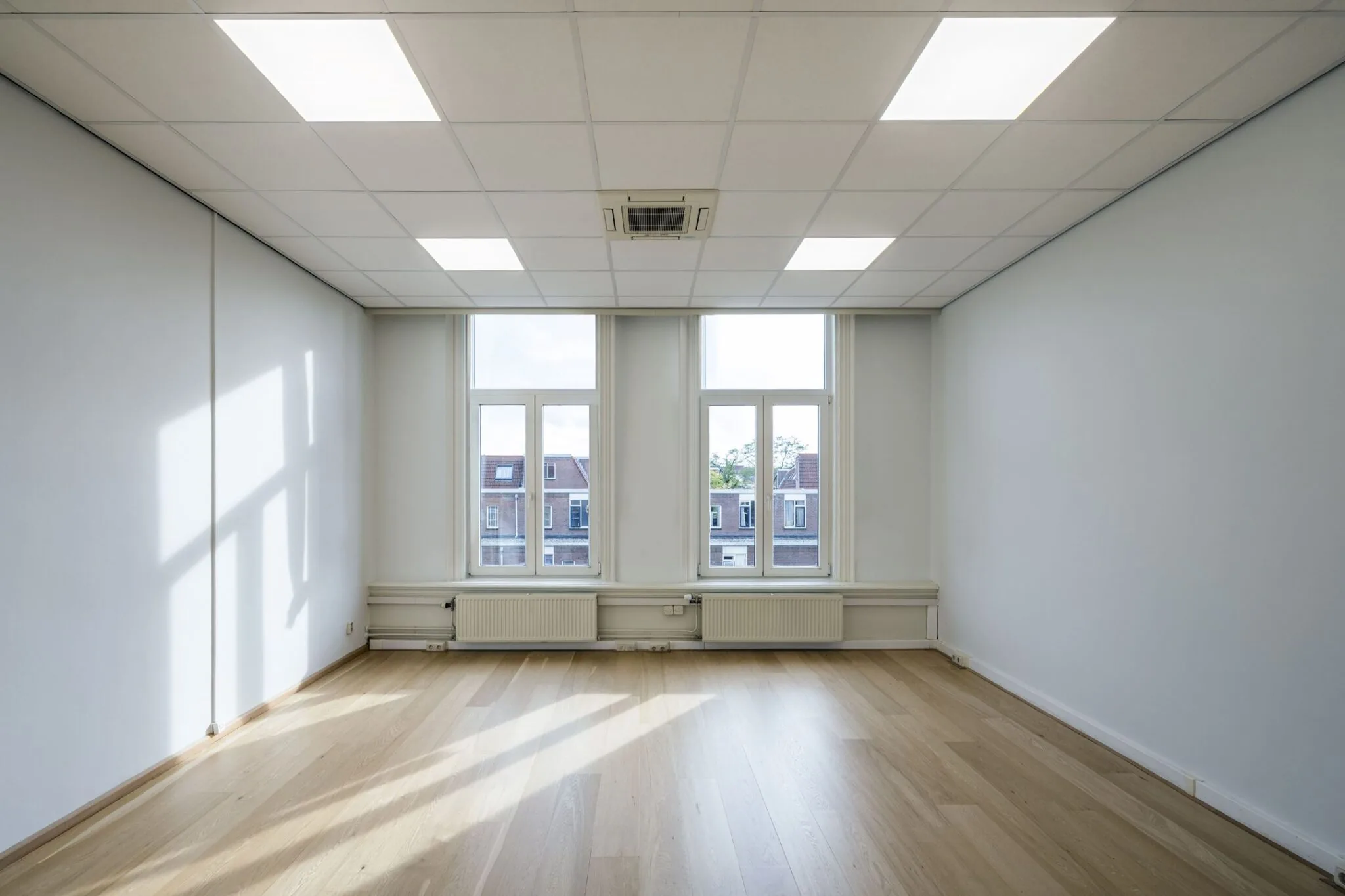 Lichte, lege kantoorruimte met houten vloer en drie hoge ramen aan de Nieuwe Gracht 45-47 in Haarlem.
