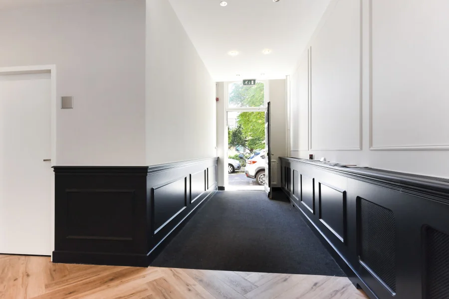 Verlichte entreehal van een kantoorruimte aan het Sweelinckplein 9-21 in Den Haag met zwarte lambrisering en zicht op de straat.