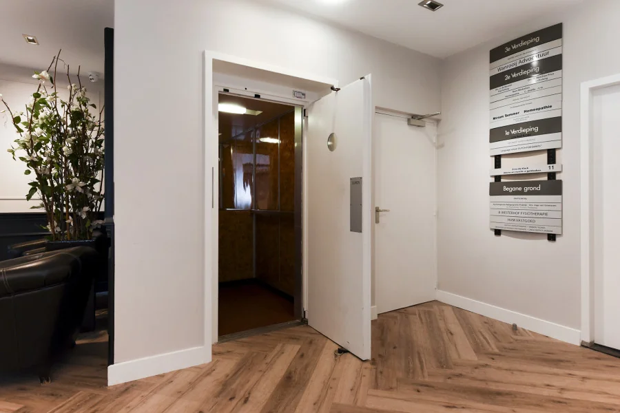 Moderne entree van een kantoorpand aan het Sweelinckplein in Den Haag met open liftdeur en duidelijke etagebewegwijzering.