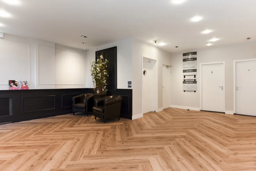 Moderne wachtruimte in een kantoorpand aan het Sweelinckplein 9-21 in Den Haag met houten visgraatvloer, zwarte balie en lederen fauteuils.